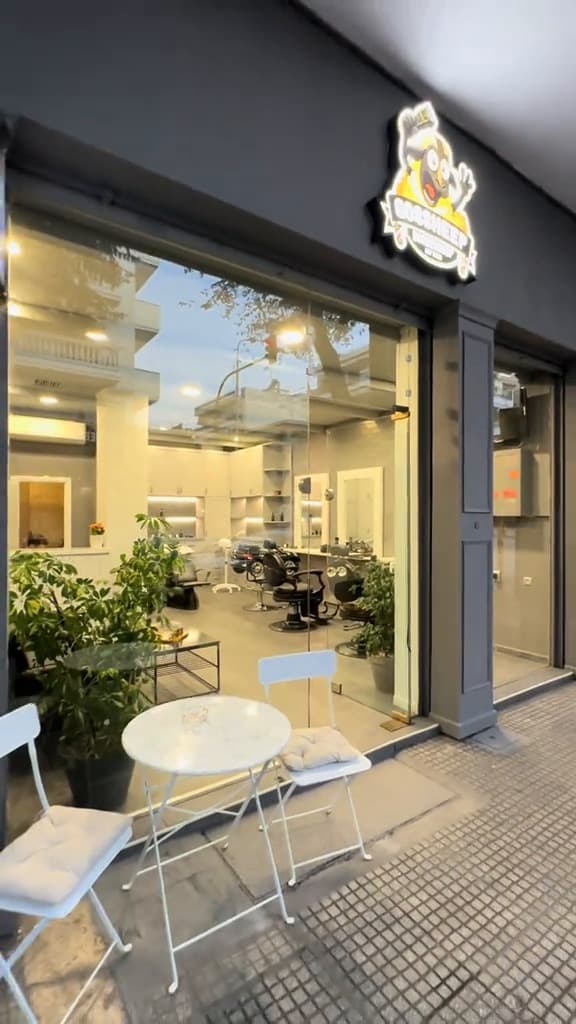 Η πρόσοψη του GOSSHEEP BARBERSHOP με τη φωτιζόμενη πινακίδα με το πρόβατο πάνω από την τζαμαρία