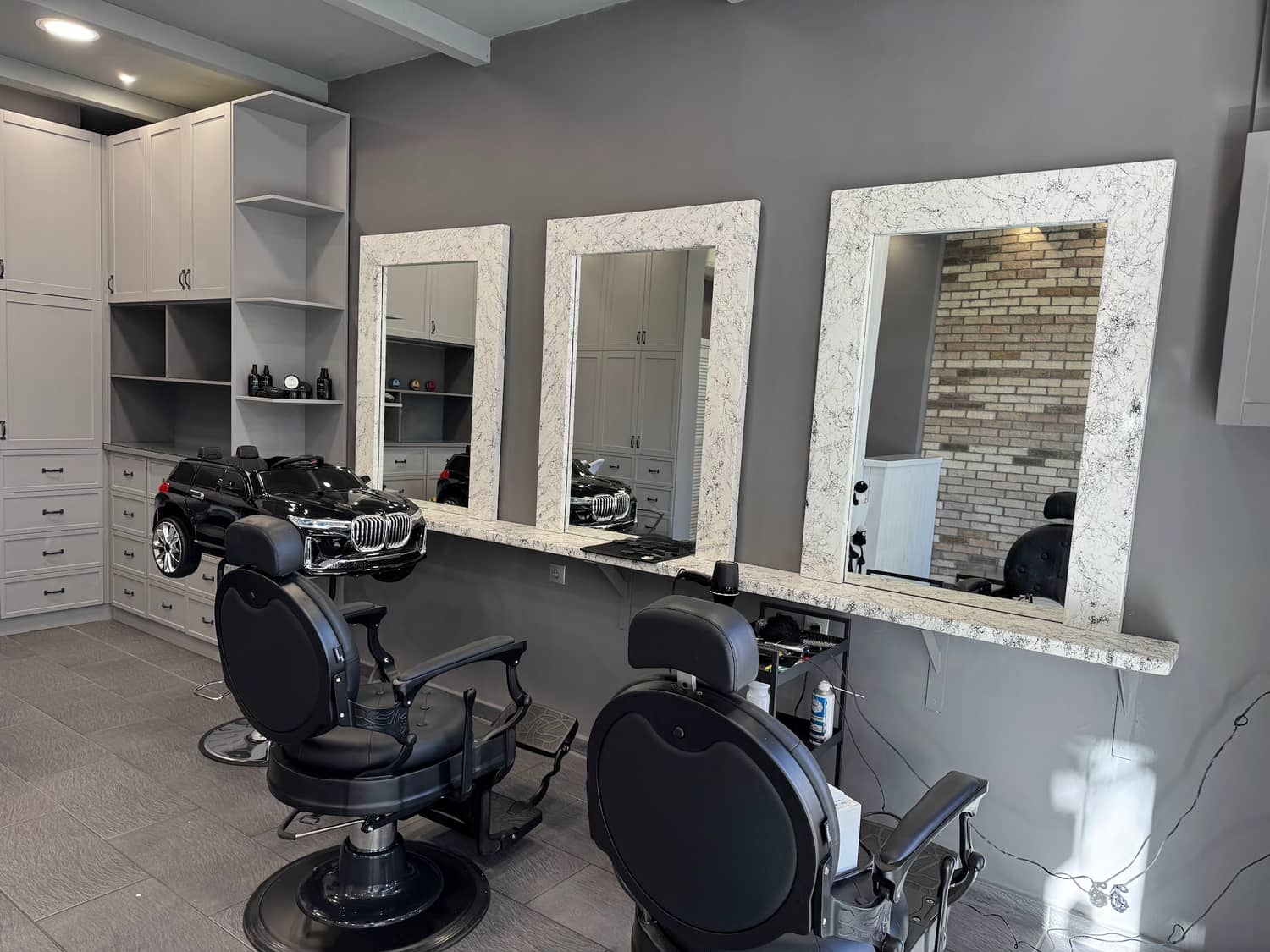 Το εσωτερικό του GOSSHEEP BARBERSHOP τη μέρα: οι τρεις καθρέφτες με το λευκό μαρμάρινο πλαίσιο, οι δύο μαύρες καρέκλες και το αυτοκινητάκι BMW για τα παιδιά
