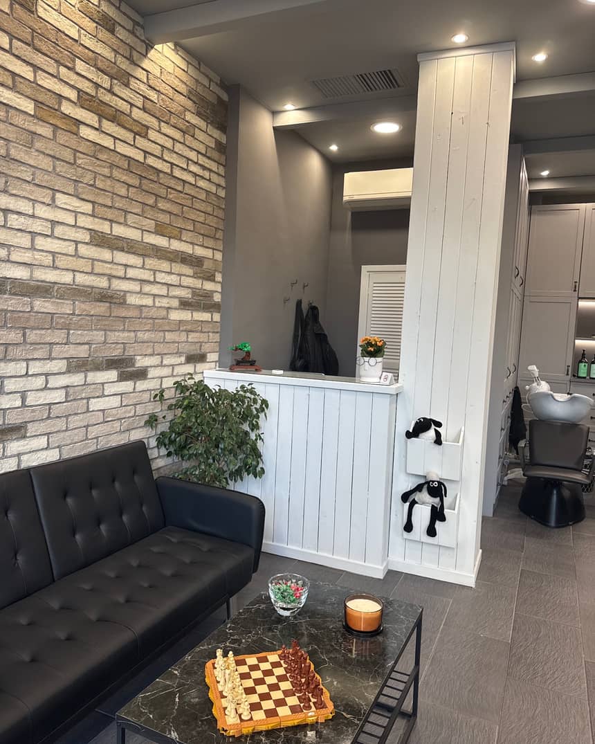 Ο χώρος αναμονής του GOSSHEEP BARBERSHOP: ο μαύρος καναπές, το σκάκι LEGO στο τραπέζι, ο τούβλινος τοίχος και τα δύο λούτρινα προβατάκια στα λευκά ράφια